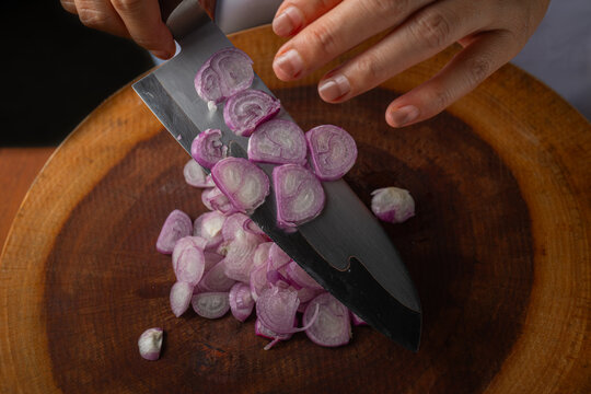 Close up of fresh sliced purple shallots sticking to chef knife blade on wooden board.