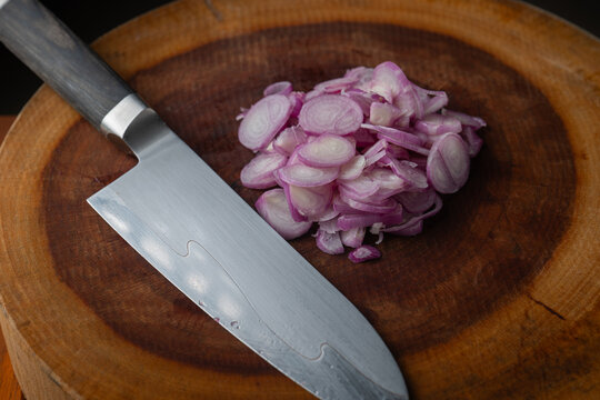Close up of sharp chef knife with pile of sliced purple shallots on wooden board.