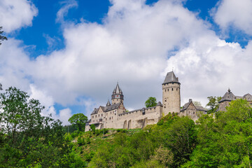 Fototapeta premium Stone Castle Towers Above Wooded Hillside and Clouds