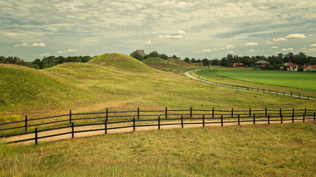 Old Uppsala, Sweden - 20.06.2026: Ancient burial mounds and rolling green hills under a cloudy sky with a wooden fence path