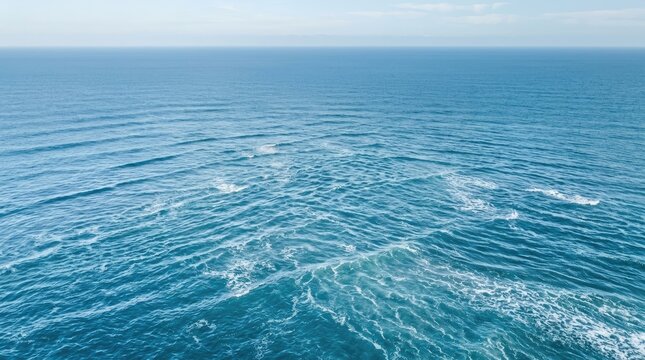 Waves roll across a vast expanse of deep blue ocean. Sunlight reflects off the water, creating white foam and ripples.