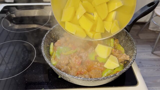Diced potatoes added to simmering meat and vegetables in pan on stove.