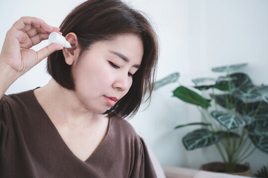Asian woman applying ear drops bottle for infection treatment or earache relief at home. Close-up shot of female putting medication into her ear canal for hearing healthcare