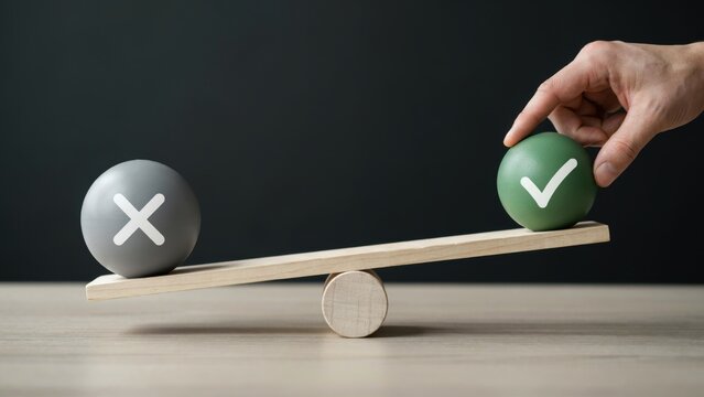 A hand balances a green sphere with a checkmark against a gray sphere with an x on a wooden scale. Conceptual metaphor for decision making.