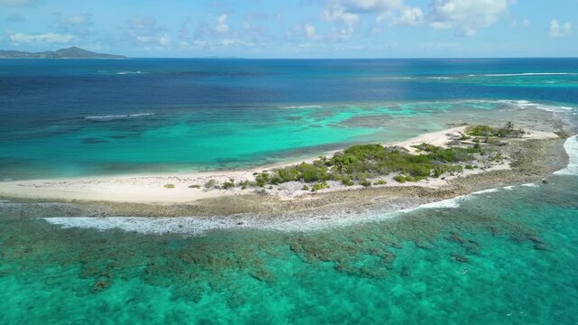 Aerial drone view shows Petit Tabac sandy island with distant Grenadines islands visible on the horizon beyond turquoise coral reef