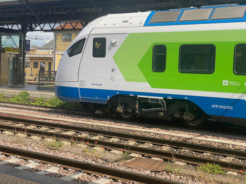 A close-up view of a contemporary Stadler ATR 803.003 train, featuring a distinctive green and blue design, waiting at a railway station