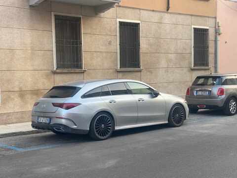 A sleek silver Mercedes-Benz CLA Shooting Brake wagon is parked next to a Mini Cooper on a narrow street with buildings in the background