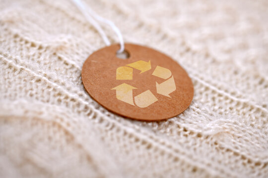 Brown craft paper clothing tag with recycling symbol on white knitted sweater