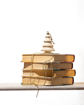 Minimalist stack of books topped with a wooden Christmas tree and gold bead garland. Perfect for eco-friendly holiday gift guides, bookstore sales, and modern academic winter promotions.