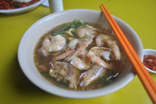 Authentic Singaporean prawn noodles (Hae Mee) with pork ribs in a rich broth, served on a yellow table at a local hawker centre 싱가포르음식 싱가폴 로컬음식