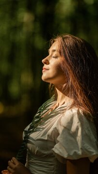 Woman with eyes closed enjoying sunlight and holding a green fern leaf