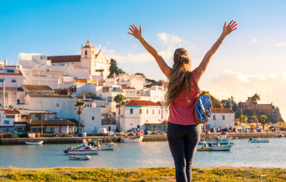 female tourist raising arms looking at ferragudo coastal village and harbor algarve portugal