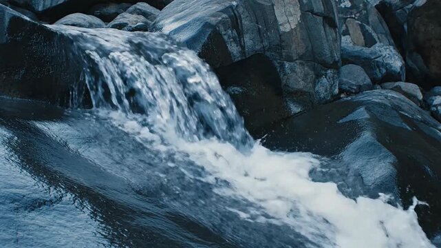 Silvered water cascades over dark smooth rocks, creating a serene natural waterfall scene.