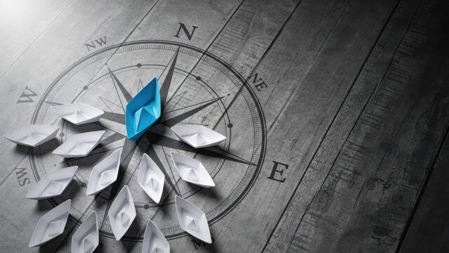 A single blue paper boat leading a fleet of white boats over a vintage compass background. Leadership concept for strategic business development.