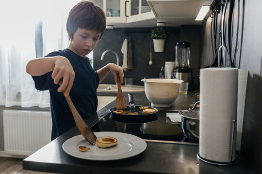 Young boy cooking pancakes in kitchen for breakfast