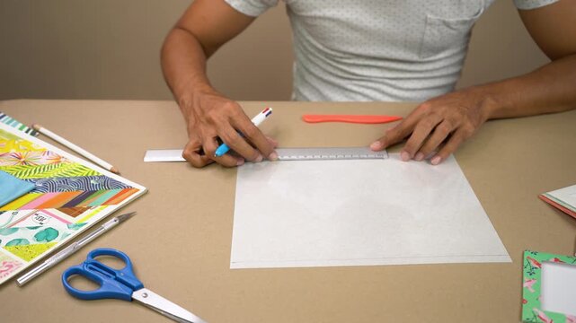 Person measuring and marking acetate sheet for crafts at tidy workspace table