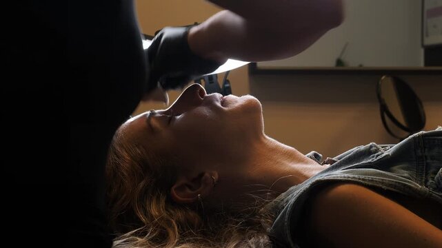 Beauty specialist cleanses the eyebrow area of a reclining woman during a permanent makeup procedure, carefully preparing and cleaning the skin, static slow motion close-up.