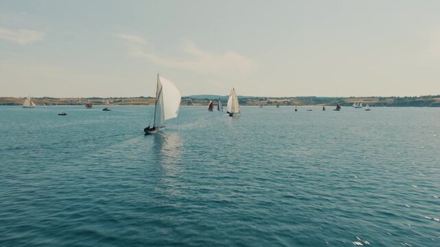 Drone overtaking classic racing sailboats under spinnaker on calm sea