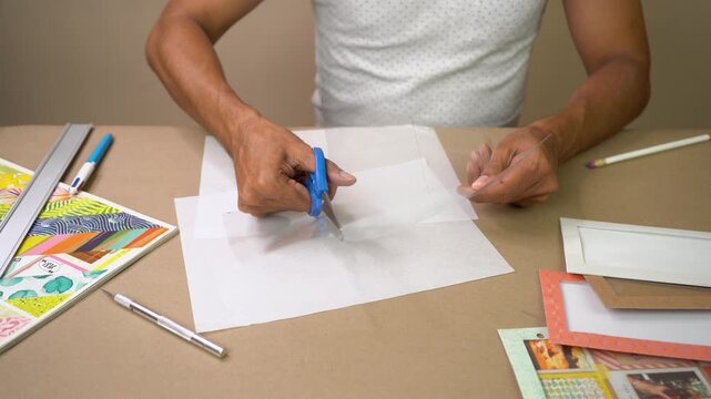 Hands cut transparent acetate with blue scissors while making handmade paper craft