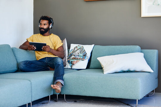 Streaming, tablet or black man on couch with headphones, song reflection or movie binge on day off. Thinking, space or person in house with tech, music perspective or watching show on weekend break.