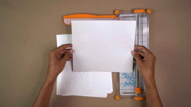 Hands position white cardstock beside paper trimmer while preparing craft project