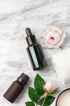 Green oil serum dropper bottle, essential oil bottle and pink rose flowers on marble table background, top view
