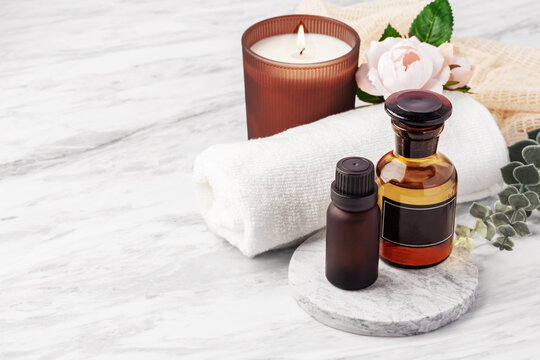 Essential oil bottles with aroma candle, and pink roses on white marble table