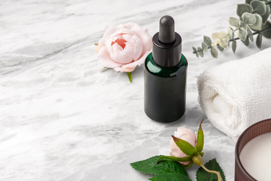 Oil serum dropper bottle or essential oil with pink rose flowers towel on marble table background, copy space