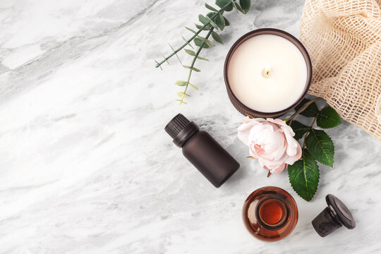Top view of essential oil bottles with aroma candle, and pink roses on white marble table, copy space