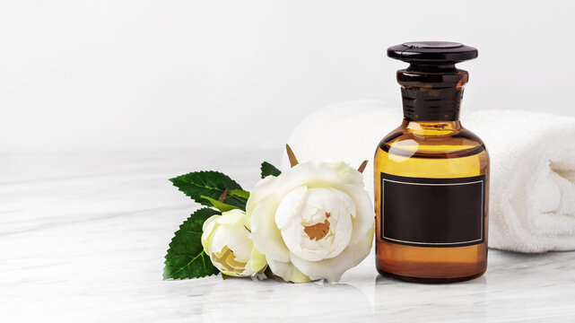 Aromatherapy essential oil bottles with blank black label,  roses flower and towel on white marble table, closeup