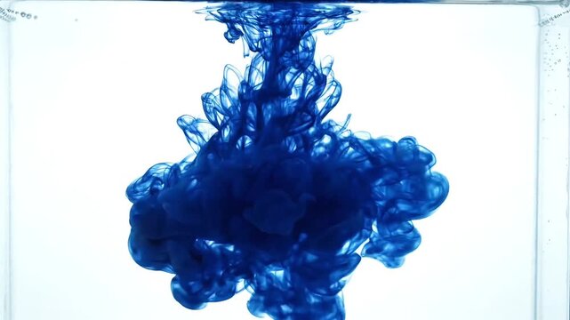 Blue ink dissolving and swirling in clear water on white background
