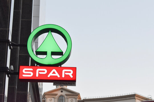 Editorial photo showing the illuminated green fir tree logo and red SPAR brand sign of a supermarket on an urban building facade in Astana, Kazakhstan, highlighting retail and commerce