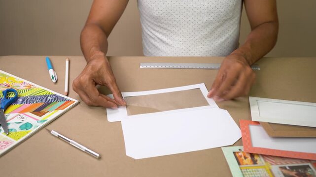 Hands assembling paper craft envelope with acetate window on work table