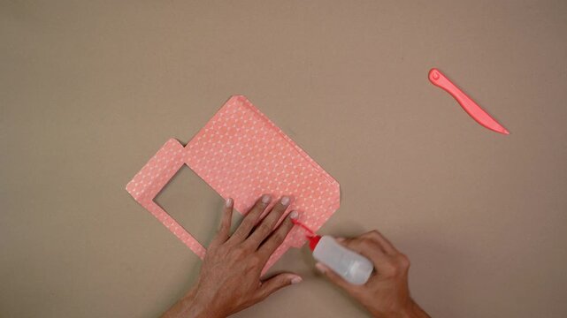 Hands gluing patterned cardstock on table with craft tools in DIY project