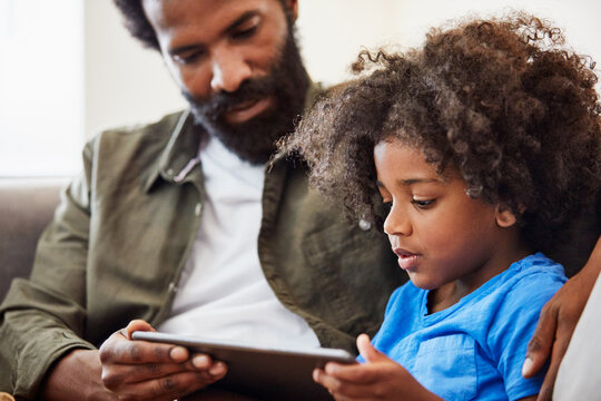 Father, child and reading with tablet in family home for language, elearning and online lesson. Black man, son and together in house for tech, literacy or kids video on education app for development