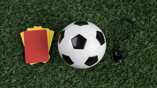 Soccer ball, referee whistle, and yellow and red cards on grass