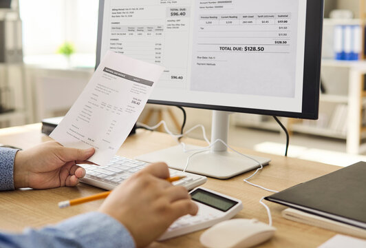Man checks bill on computer with calculator. Home office with utility invoice and documents. Budget planning, finance, payment and expenses tracking. Clear concept of household budgeting.