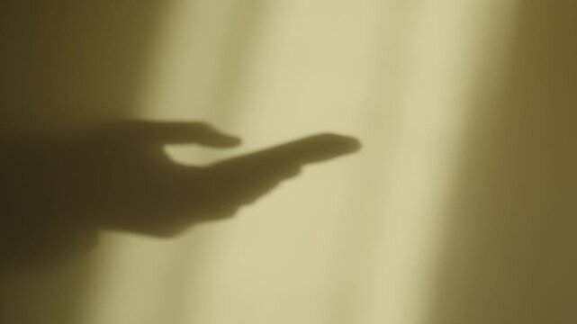 Close up of shadow on a wall of hands holding using smartphone mobile typing and scrolling or making a phone call or sending text message. Business deal. Suspicious criminal activity. Male silhouette