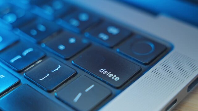 Close up on finger pressing the Delete keypad on laptop computer keyboard in office or home. Dark room at night as person erases files from system or cleaning data. Urgent removal by hacker or user