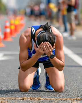 Exhaustion at the Finish Line A runner collapses to their knees, hands covering their face in a moment of sheer exhaustion and emotional release after completing a demanding race.