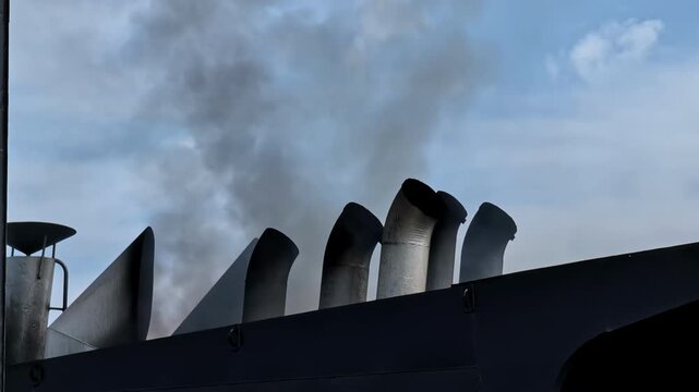 Ship smokestacks release smoke above a dark deck edge in Riga, Latvia.