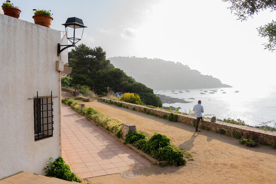 Man standing on a sunny coastal path overlooking the tranquil Mediterranean sea and fishing boats in a Spanish bay