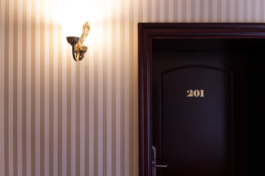 Hotel room door with room number 201 in a hallway, featuring a decorative wall sconce illuminating striped wallpaper