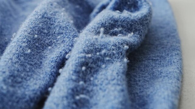 Pilling  on blue knitted sweater, showing worn textile texture, fuzzy fibers.  Pilled sweater close up. Detailed textile texture.  Clothing care and textile quality concept 