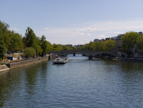 Seine River cruise boat sailing past city architecture and lush trees in Paris