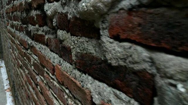 High-resolution tracking shot moving forward along a rustic, weathered red brick wall. This first-person perspectiveHighlights the rough mortar joints and coarse texture of the exposed bricks as the c