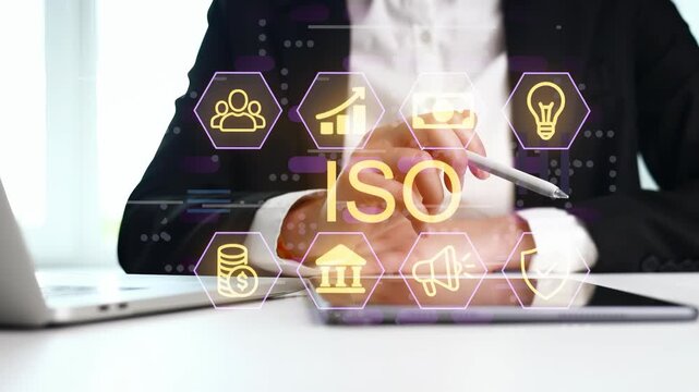 A business professional sits in an office and discusses ISO standards using a tablet and a laptop. Digital graphics appear on the screen to illustrate key points during the meeting.