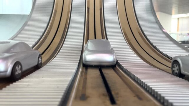 Miniature silver cars navigate parallel sloped wooden tracks, vehicle movement, modern exhibition.
