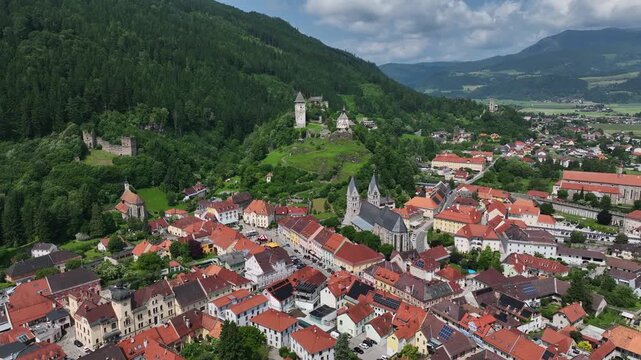 Summer drone footage showing medieval Friesach, old fortified walls, rooftops, towers, hills, serene atmosphere, warm daylight, gentle cinematic motion