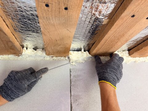 A builder trims expanding polyurethane foam where a wall and ceiling meet.